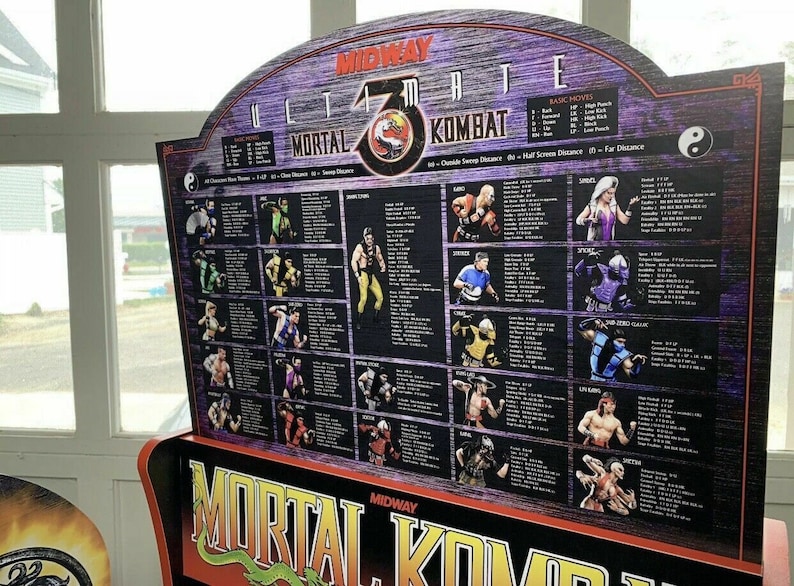 May include: A close-up of a Mortal Kombat 3 arcade game cabinet. The cabinet is purple and black with a large image of the game's logo. The cabinet has a list of characters and their moves on the side. The text on the cabinet reads "Ultimate Mortal Kombat 3".