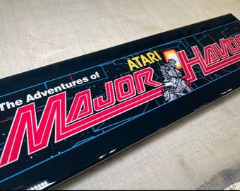 May include: A black and red arcade game control panel with the text "The Adventures of Major Havoc" and "ATARI" on it. The panel features a stylized image of a robot.
