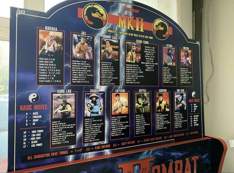 May include: A blue and black Mortal Kombat II arcade game cabinet with a character select screen. The screen shows the characters Baraka, Jax, Johnny Cage, Shang Tsung, Kitana, Mileena, Kung Lao, Raiden, Liu Kang, Reptile, Scorpion, and Sub-Zero. The cabinet also has a list of basic moves and a description of the characters' special moves.