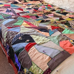 May include: A colorful patchwork quilt with a variety of fabric patterns and colors, including red, blue, green, and brown. The quilt is spread over a bed, showcasing its intricate design and craftsmanship. The quilt's dimensions are not visible.
