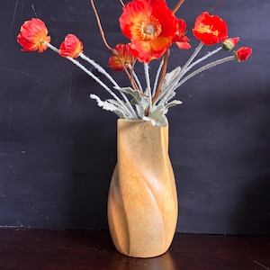 May include: A tall, light orange ceramic vase with a spiraling, twisted vertical design. The vase is filled with a bouquet of bright red poppy flowers featuring yellow centers and thin, fuzzy, light gray stems and green leaves.
