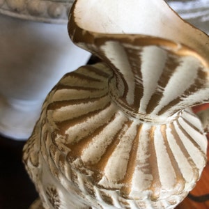 May include: White ceramic vase with gold accents. The vase has a fluted design and a wide mouth.