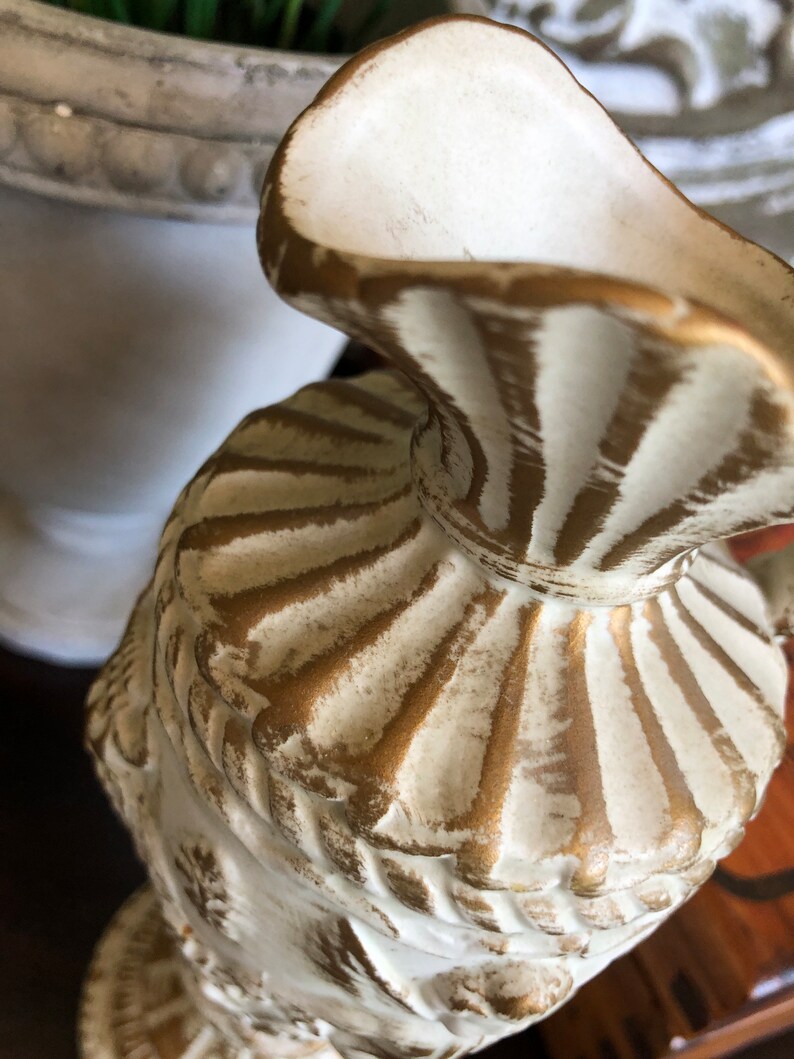 May include: White ceramic vase with gold accents. The vase has a fluted design and a wide mouth.
