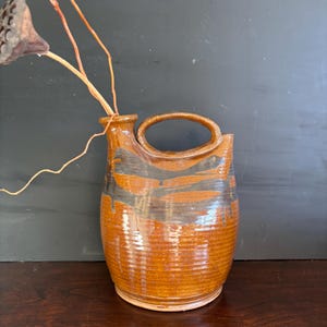 May include: A brown ceramic pitcher with a black glaze design. The pitcher has a rounded body and a handle.