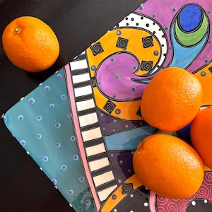 May include: A rectangular ceramic serving platter featuring a vibrant, multi-colored abstract pattern with teal, purple, orange, and black accents, including polka dots, stripes, and swirls, displayed with three fresh, round, bright orange citrus fruits.