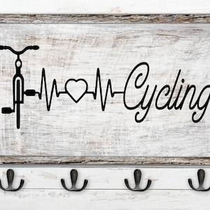 Puede incluir: Un letrero de madera blanco con una silueta negra de una bicicleta y una línea de latido del corazón con la palabra "Cycling" en una fuente cursiva.
