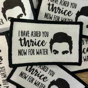 May include: White rectangular patches with black borders and the text "I HAVE ASKED YOU thrice NOW FOR WATER" in black. Each patch features a black silhouette of a person's face. Patches are stacked.