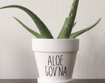 May include: A white ceramic mug with a black handle and the text "But first, coffee" in a black, handwritten-style font. The mug is on a white surface.