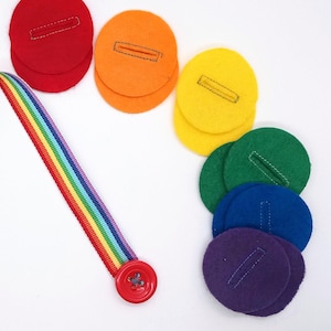 May include: A rainbow-colored felt strip with a red button at the end. The strip is attached to a set of felt circles in rainbow order, each with a slit cut out.