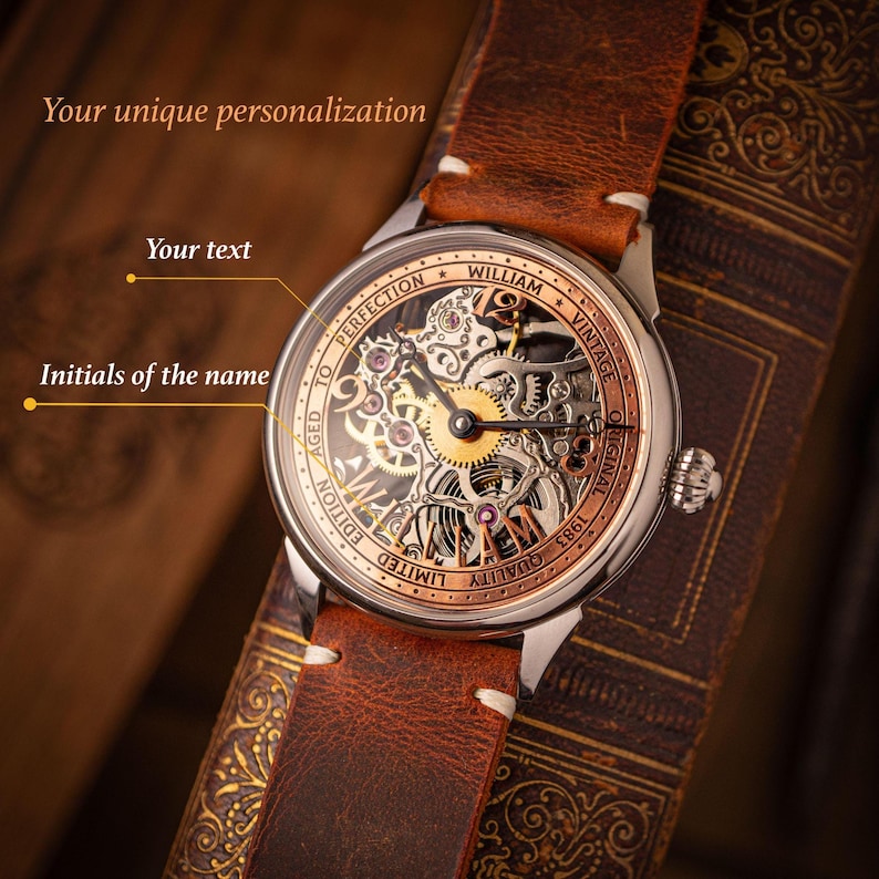 May include: A vintage wristwatch with a brown leather strap. The watch face has a skeleton design, revealing the internal mechanisms. The watch has a silver case with gold and copper detailing. The text on the watch face includes "WILLIAM VINTAGE ORIGINAL 1983 QUALITY LIMITED EDITION AGED TO PERFECTION".
