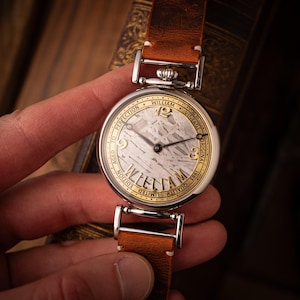 May include: A vintage-style wristwatch with a silver case and a brown leather strap. The watch face features the name "WILLIAM" and the words "VINTAGE" and "ORIGINAL". The watch has a unique textured face and a silver case with a brown leather strap.