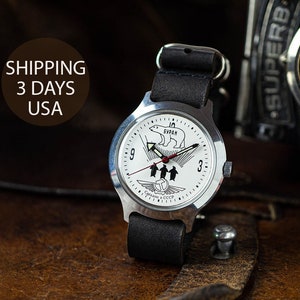 May include: A silver wristwatch with a white face and black leather band. The watch face features a polar bear graphic and the text "БУРАН".