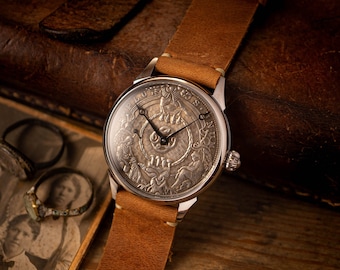 May include: A silver pocket watch with a brown leather strap. The watch face features an intricate design with Roman numerals and a detailed image of a mythical creature.