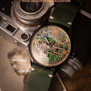 May include: A close-up of a black wristwatch with a green leather strap. The watch face features a map design with the Statue of Liberty and the text "NY". The watch also has the text "HANDCRAFTED AND SKELETONIZED MECHANISMS" and "YOUR UNIQUE PERSONALIZATION".