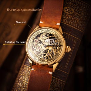 Op de afbeelding: Een goudkleurig vintage horloge met een bruine leren band. De wijzerplaat van het horloge toont zichtbare tandwielen en de tekst "WILLIAM VINTAGE ORIGINAL 1983". Het horloge wordt gepresenteerd op een vintage boek. De tekst "Your unique personalization", "Your text" en "Initials of the name" is inbegrepen.