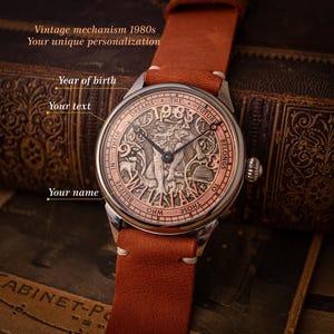 Puede incluir: Un reloj de pulsera de estilo vintage con una esfera de color cobre y una correa de cuero marrón. La esfera presenta un diseño detallado con el año 1983 y el texto "Dreams * The Future Belongs To Those Who Believe In Their Own Will Name".