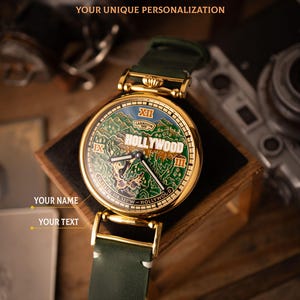 May include: A gold-toned wristwatch with a green leather strap. The watch face features a map of Hollywood in green and blue, with the word "HOLLYWOOD" prominently displayed. The text "HANDCRAFTED AND SKELETONIZED MECHANISMS YOUR UNIQUE PERSONALIZATION" is at the top.
