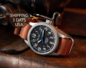 May include: A silver aviator watch with a black face and brown leather band. The watch face has white numbers and a blue second hand. The watch has a 24-hour scale and the words "AVIATOR" and "17 JEWELS" printed on the face.