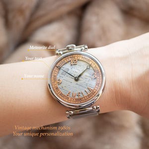 May include: A silver wristwatch with a white meteorite dial and rose gold accents. The watch face features the text "The future belongs to those who believe in their dreams".