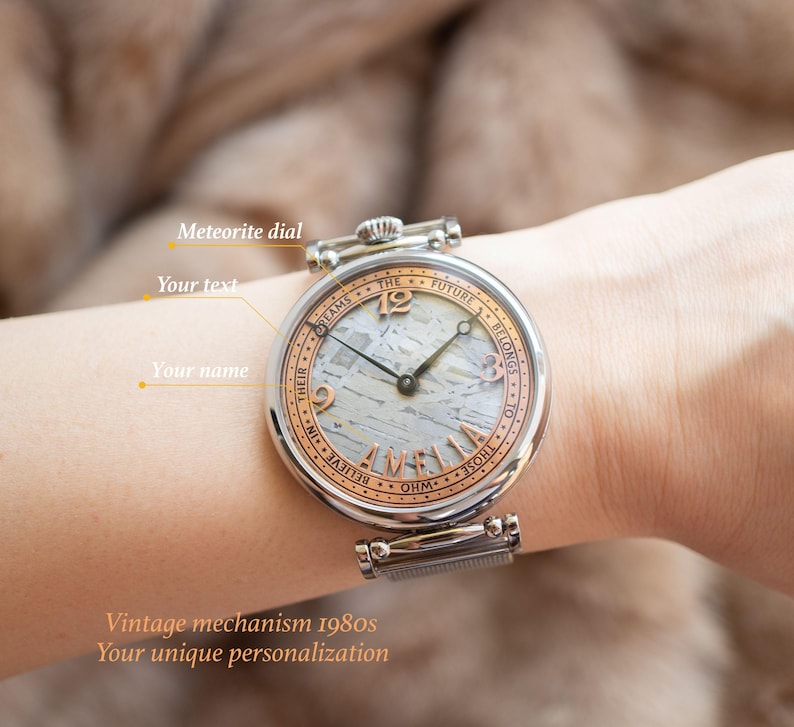 May include: A silver wristwatch with a white meteorite dial and rose gold accents. The watch face features the text "The future belongs to those who believe in their dreams".