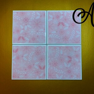 Peut inclure: Ensemble de quatre sous-verres en c&eacute;ramique rose et blanche avec un motif de flocon de neige et de feuilles de houx.
