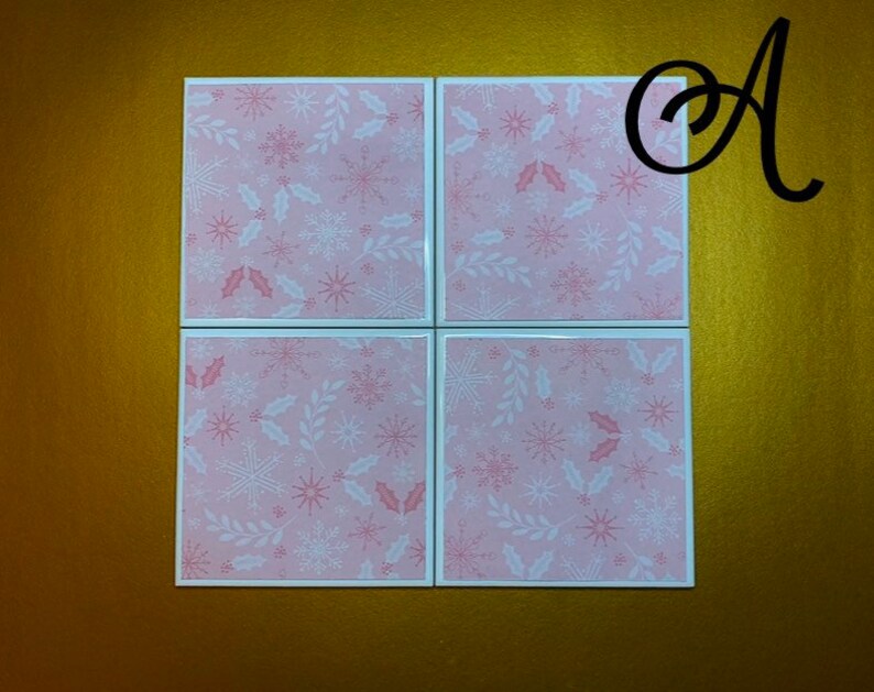 Peut inclure: Ensemble de quatre sous-verres en c&eacute;ramique rose et blanche avec un motif de flocon de neige et de feuilles de houx.