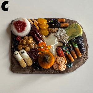 Op de afbeelding: Een miniatuur Halloween-charcuteriebord met een verscheidenheid aan etenswaren, waaronder kaas, crackers, fruit en snoep. Het bord is gemaakt van bruin klei en heeft een rustieke uitstraling.