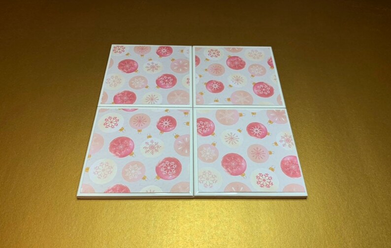 Peut inclure: Ensemble de quatre sous-verres en c&eacute;ramique blanche avec un motif d'ornements roses et dor&eacute;s.