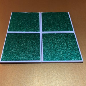 Peut inclure: Ensemble de quatre sous-verres carr&eacute;s en paillettes vertes avec des bordures blanches.