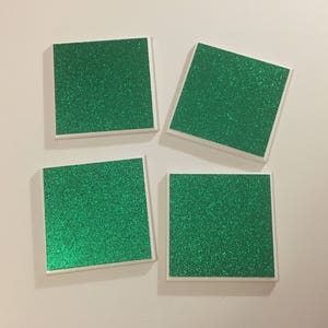 May include: Four square coasters with a white border and a green glitter surface.