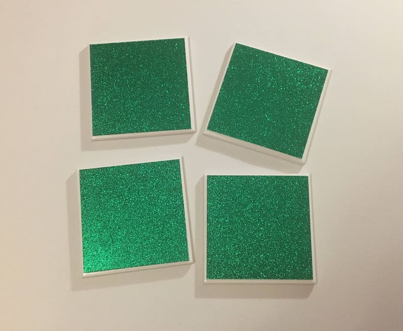May include: Four square coasters with a white border and a green glitter surface.