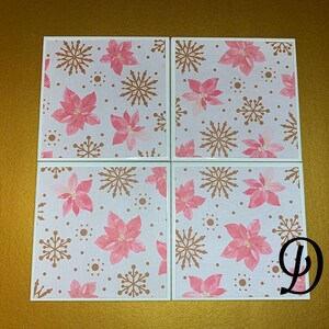 Peut inclure: Ensemble de quatre sous-verres en c&eacute;ramique blanche avec un motif de poinsettia rose et de flocons de neige dor&eacute;s.
