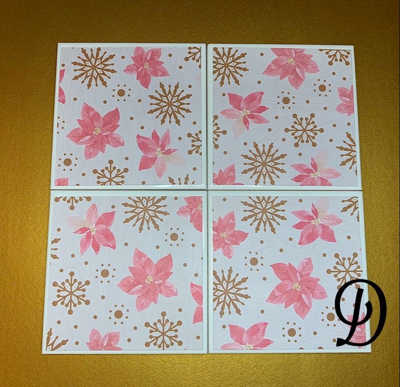 Peut inclure: Ensemble de quatre sous-verres en c&eacute;ramique blanche avec un motif de poinsettia rose et de flocons de neige dor&eacute;s.