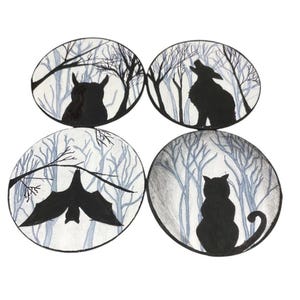 Pode incluir: Quatro ilustra&ccedil;&otilde;es circulares com silhuetas pretas de animais da floresta. Uma coruja, um lobo uivando, um morcego e um gato s&atilde;o retratados em um fundo de &aacute;rvores nuas. A obra de arte &eacute; em preto e branco.