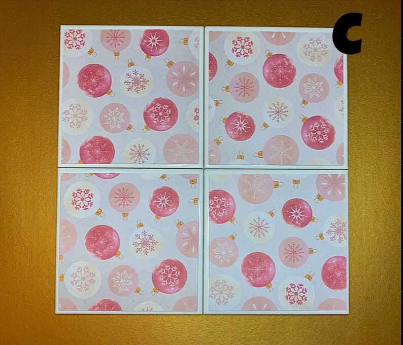 Peut inclure: Quatre sous-verres carr&eacute;s en c&eacute;ramique rose et blanche avec un motif r&eacute;p&eacute;t&eacute; de boules roses et de flocons de neige blancs.