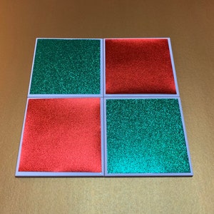 Peut inclure: Quatre sous-verres carr&eacute;s avec une finition paillet&eacute;e. Deux sous-verres sont rouges et deux sont verts.