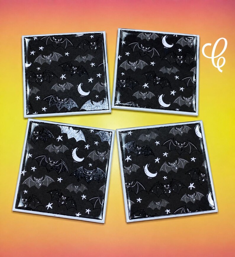 May include: Four square coasters featuring a repeating pattern of black bats, white crescent moons, and white stars on a black background. Each coaster has a glossy finish and a white border, arranged in a two-by-two grid formation.