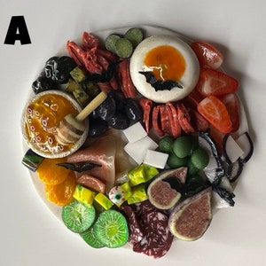 Op de afbeelding: Een witte serveerschaal met verschillende etenswaren die in een decoratief patroon zijn gerangschikt. De schaal bevat fruit, kaas, crackers en andere snacks. Het eten is op een visueel aantrekkelijke manier gerangschikt, met de nadruk op kleur en textuur.