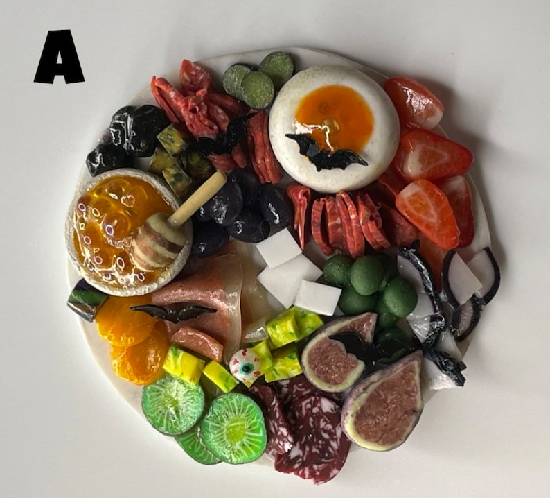 Op de afbeelding: Een witte serveerschaal met verschillende etenswaren die in een decoratief patroon zijn gerangschikt. De schaal bevat fruit, kaas, crackers en andere snacks. Het eten is op een visueel aantrekkelijke manier gerangschikt, met de nadruk op kleur en textuur.