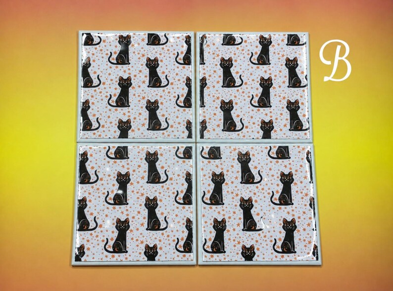 May include: Four square ceramic coasters featuring a repeating pattern of black cats on a white background with small orange stars. The letter B is printed in white in the upper right corner. Each coaster has a glossy finish and a light grey border.