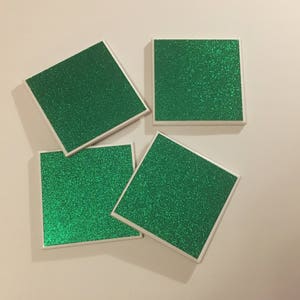 May include: Four square green glitter coasters with white borders.