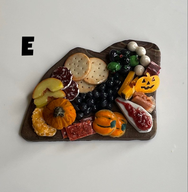 Op de afbeelding: Een miniatuur charcuterie-bord met een verscheidenheid aan herfstthema-voedingsmiddelen, waaronder crackers, salami, kaas, druiven, pompoenen en een schijf fruit. Het bord is gemaakt van donkerbruin hout en heeft een rustieke uitstraling.
