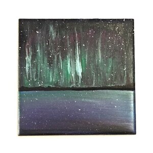 Puede incluir: Un azulejo de cer&aacute;mica pintado a mano que representa una escena de agua azul oscuro y p&uacute;rpura con una aurora boreal verde y blanca en el cielo nocturno.