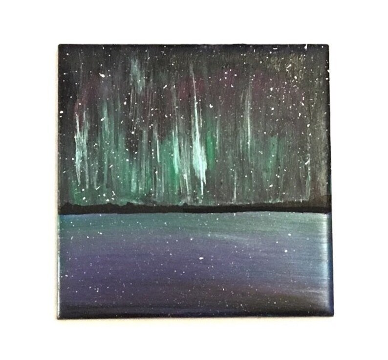 Puede incluir: Un azulejo de cer&aacute;mica pintado a mano que representa una escena de agua azul oscuro y p&uacute;rpura con una aurora boreal verde y blanca en el cielo nocturno.