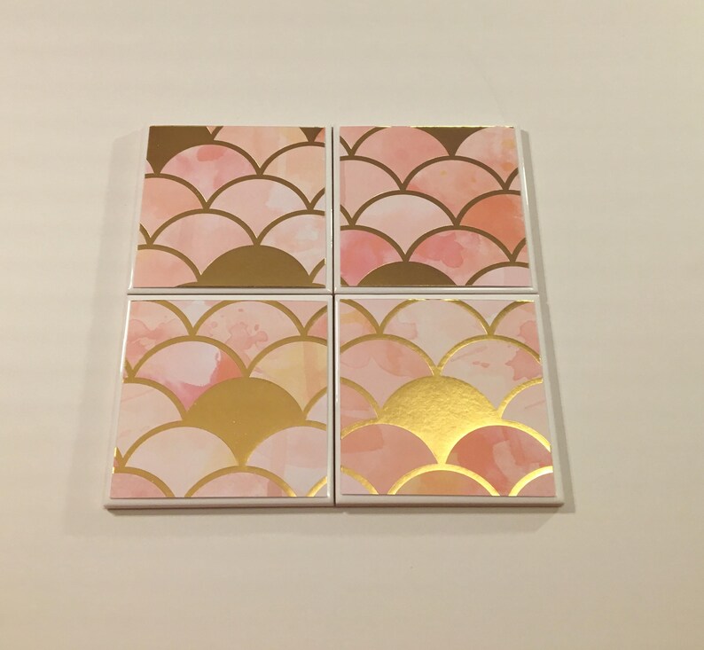 K&ouml;nnte beinhalten: Satz mit vier quadratischen Untersetzern mit einem rosa-goldenen Aquarelldesign. Das Design zeigt ein sich wiederholendes Muster aus &uuml;berlappenden Halbkreisen.