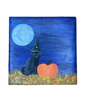 Op de afbeelding: Een vierkant schilderij toont een zwarte kat met een heksenhoed naast een oranje pompoen. Een grote blauwe maan en een sterrenhemel vormen de achtergrond. De kat zit in een veld met bruin en geel gras.
