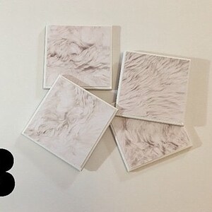 May include: Four square white coasters with a faux fur texture. The coasters are arranged in a pile.