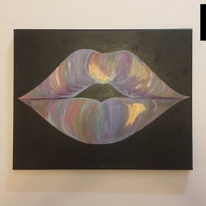 May include: A rectangular canvas painting featuring a pair of lips centered on a solid black background. The lips are rendered with blended strokes of iridescent purple, blue, pink, and gold paint, creating a shimmering, multi-colored effect.