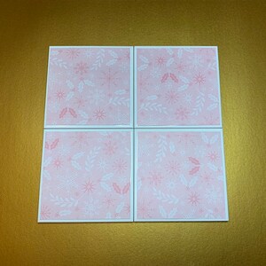 Peut inclure: Quatre sous-verres carr&eacute;s roses avec un motif de flocons de neige et de feuilles de houx blancs.