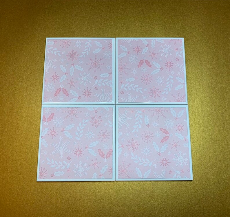 Peut inclure: Quatre sous-verres carr&eacute;s roses avec un motif de flocons de neige et de feuilles de houx blancs.
